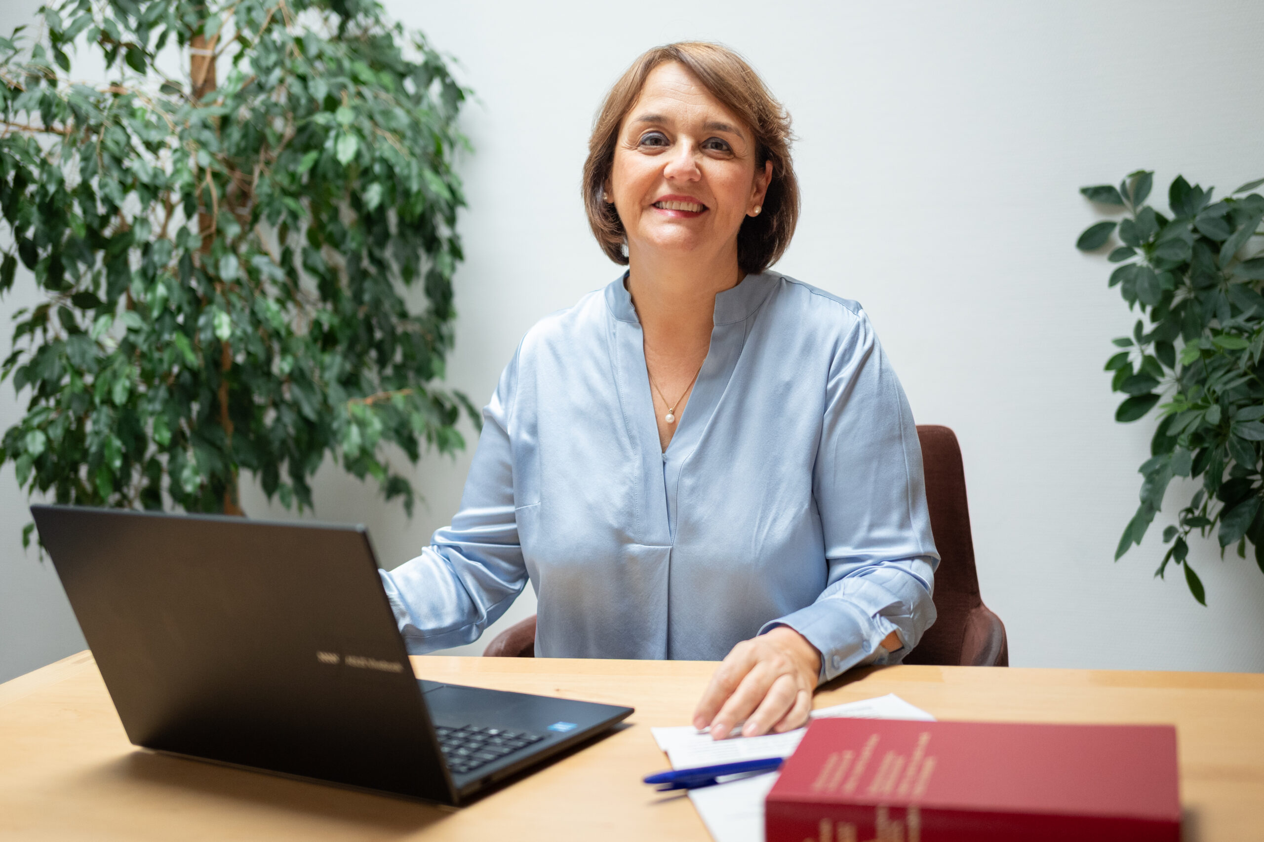 Frau sitzt am Tisch mit Laptop und Buch